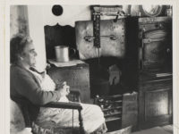 A person sitting beside an old-fashioned oven