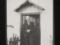 A man in a suit standing in front of his front door.