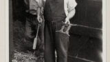 Male informant holding a smithy-made horse gag, in the doorway of stables at Finghall ( Wensleydale).