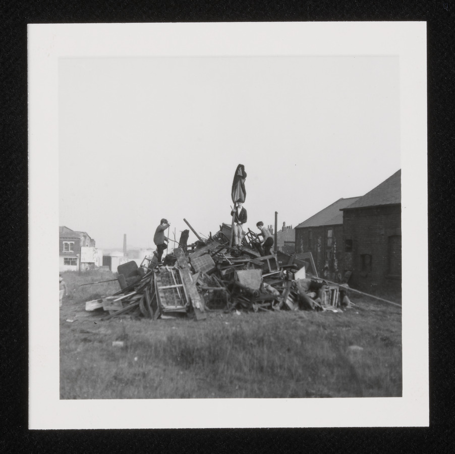 Two children clambering on a heap of wood for a bonfire.